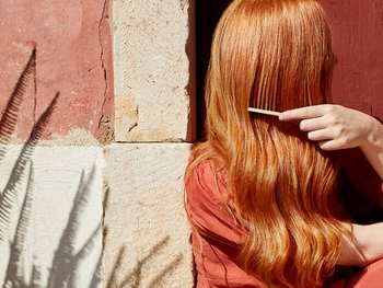 Frau auf einer Treppe, die sich ihre langen rote Haare kämmt