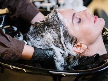 Dunkelhaarige Frau, die lächelnd eine Haarkur auf ihr nasses Haar auftragen lässt