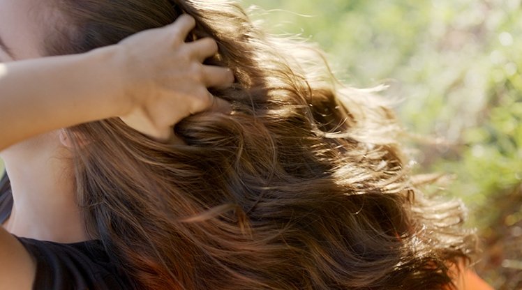 Eine Frau fasst sich in ihre langen welligen braunen Haare