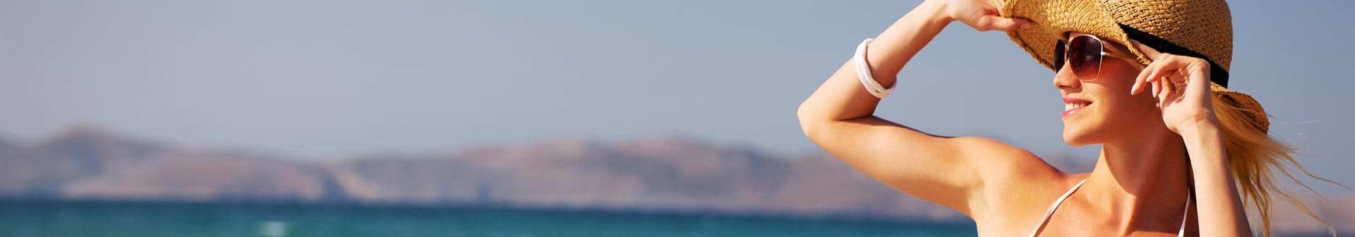 Frau im Bikini und Sonnenhut schaut aufs Meer hinaus