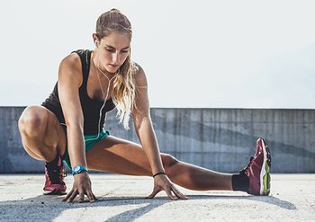 Eine Frau dehnt ihre Beine nach dem Ausdauersport – Stretching für schlanke, gestraffte Oberschenkel