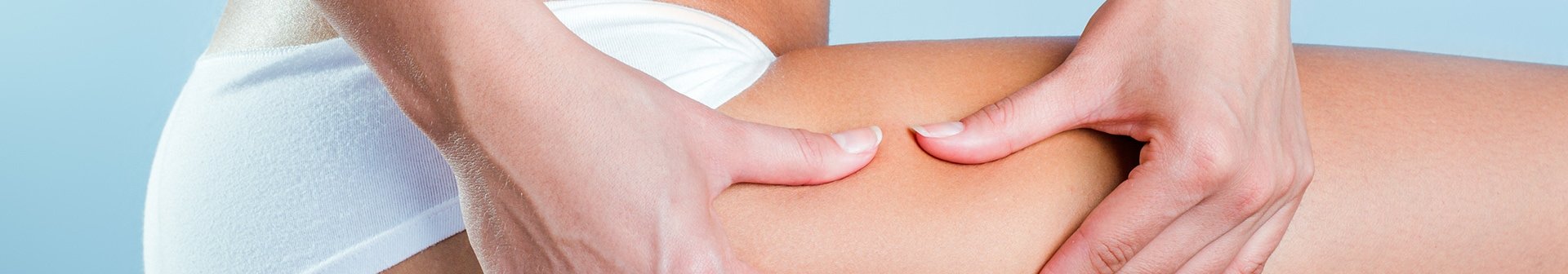 Eine Frau mit weißem Slip fasst sich an den Oberschenkel, um Cellulite zu zeigen