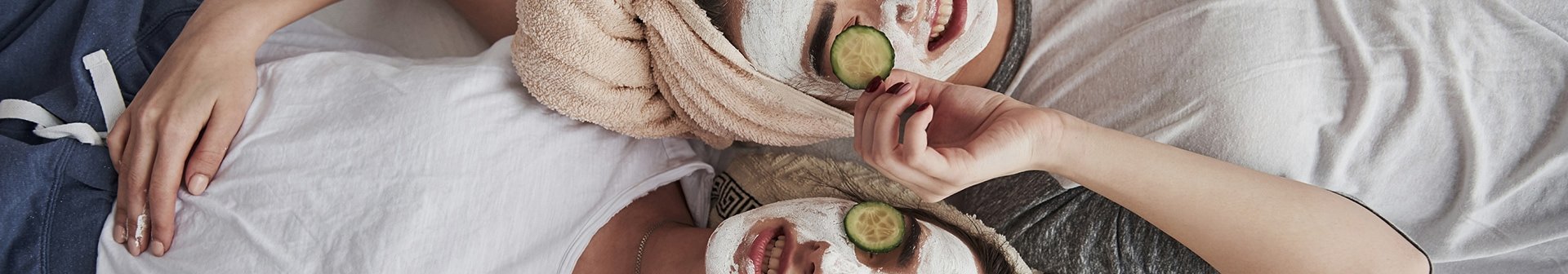 Zwei Frauen mit Gesichtmasken mit Gurkescheiben liegen auf einem Bett