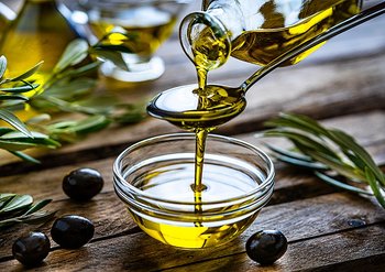 Olivenöl aus einer Flasche wird in eine Glasschale gegossen