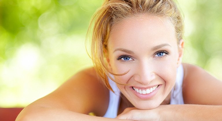 Junge Frau stützt Ihren Kopf mit dem Kinn auf ihre Hände, lächelnd