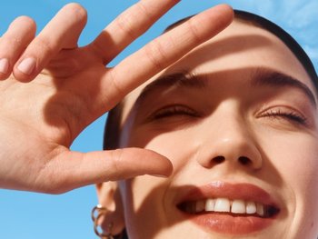 Junge Frau schützt ihr Gesicht mit der Hand vor starker Sonneneinstrahlung