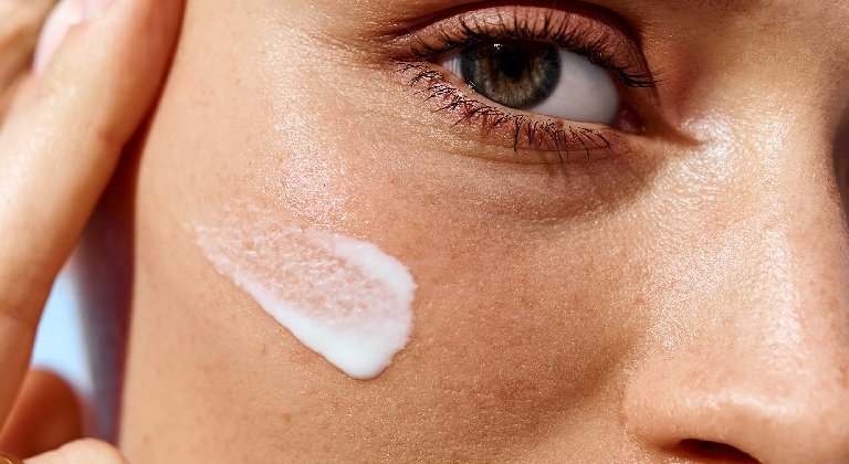 Frau trägt Sonnenschutzcreme auf ihr Gesicht auf, um sich vor Hautalterung durch Sonne zu schützen