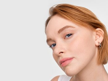 Junge Frau trägt Sonnenschutzcreme auf das Gesicht auf, um Hautschäden durch UV-Strahlen zu vermeiden