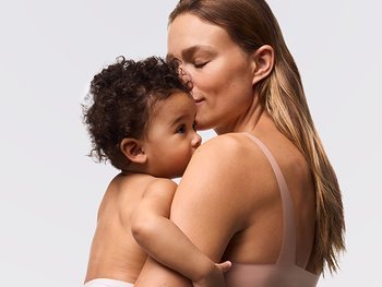 Mutter hält ihr Baby im Arm, dessen empfindliche Babyhaut vor Hautschäden durch Sonne geschützt werden muss