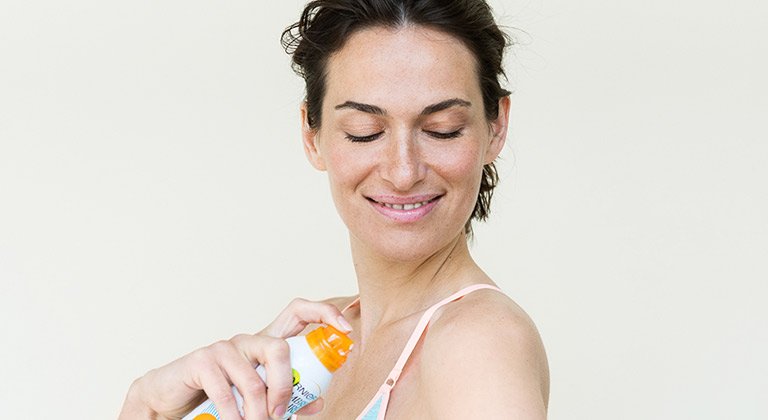 Frau sprüht Sonnenspray auf ihre Haut