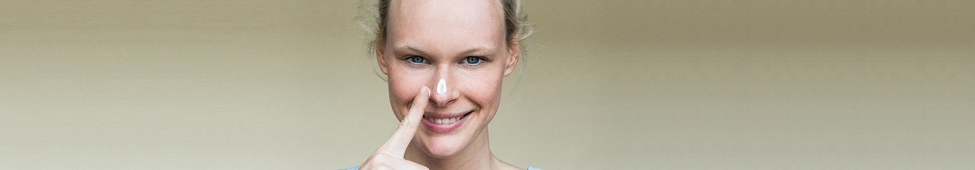 Lächelnde Frau mit Sonnencreme auf der Nase