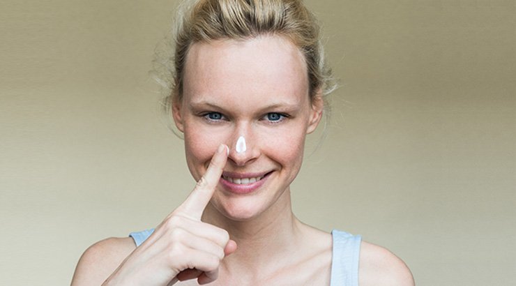 Lächelnde Frau mit Sonnencreme auf der Nase