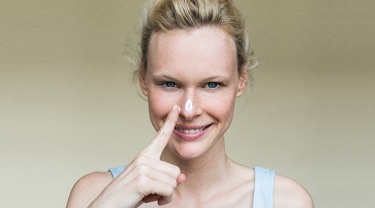 Lächelnde Frau mit Sonnencreme auf der Nase