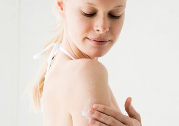 Frau reibt Sonnencreme auf ihren Arm