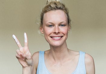Frau macht das Friedenszeichen mit Sonnencreme auf den Fingern