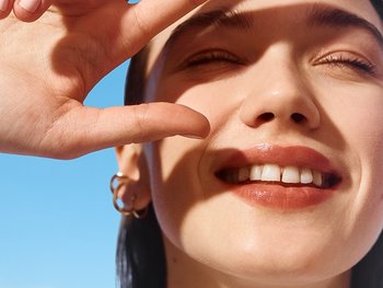 Frau die drei Finger vor ihr gesonntes Gesicht hält