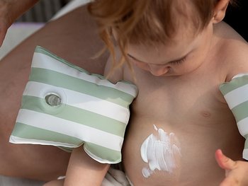 Baby, dass auf seinen mit Sonnencreme bedeckten Bauch schaut