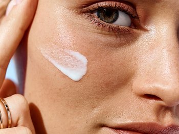 Gesicht einer Frau mit einem Streifen Sonnencreme auf ihrer rechten Wange