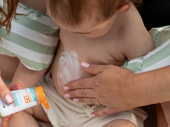 Mutter, die ihrem Baby Sonnencreme auf den Bauch aufträgt