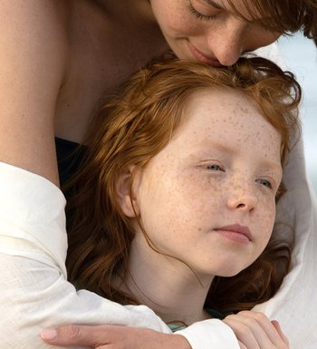 Kleines Mädchen wird von hinten von ihrer Mutter umarmt