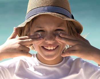 Lächelndes Kind in der Sonne schmiert sich Sonnencreme auf die Wangen