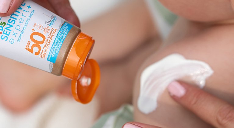 Auf die Schulter eines Kindes wird Sonnenschutz aufgetragen