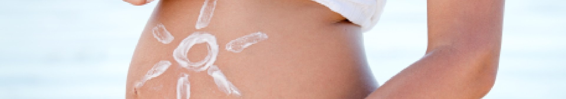 Schwangere Frau malt mit Sonnencreme eine Sonne auf den Bauch