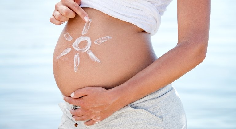Schwangere Frau malt mit Sonnencreme eine Sonne auf den Bauch