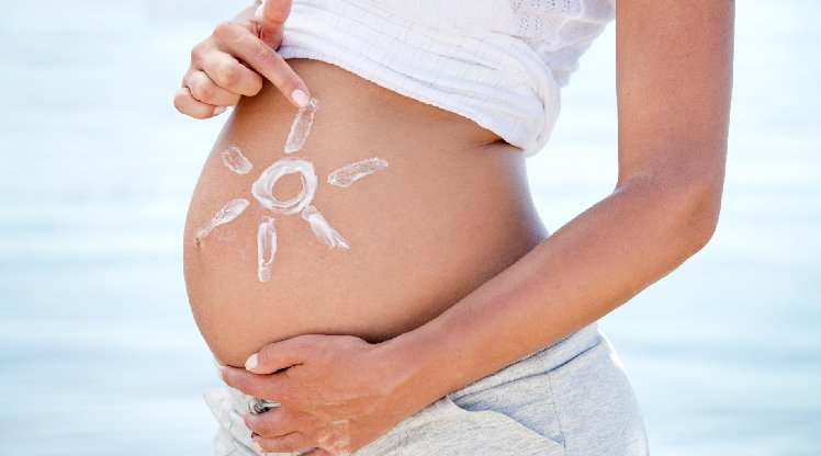 Schwangere Frau malt mit Sonnencreme eine Sonne auf den Bauch
