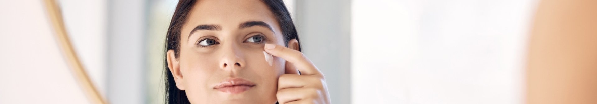Frau blickt in einen Spiegel und trägt Sonnencreme unter Make-up auf