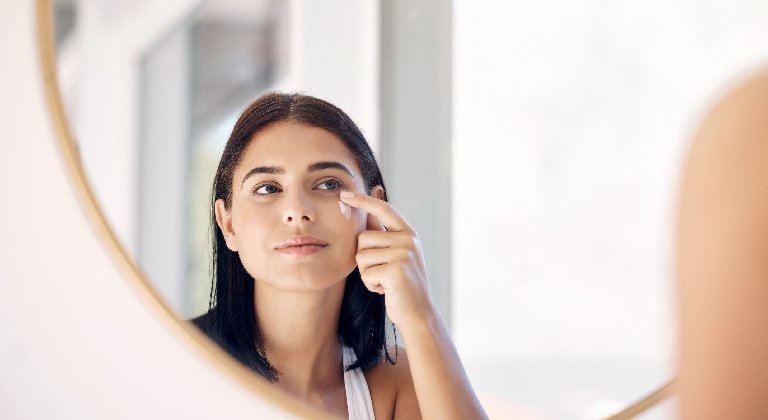 Frau blickt in einen Spiegel und trägt Sonnencreme unter Make-up auf