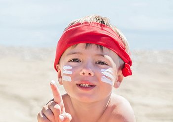 Kind am Strand mit Sonnencreme auf den Wangen