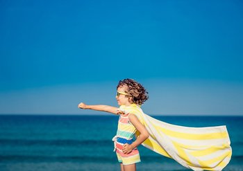 Kind am Meer mit Handtuch-Cape, UV-Kleidung und Sonnenbrille