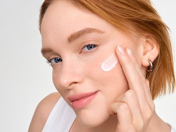 Junge Frau trägt Sonnenschutzcreme auf Gesicht auf