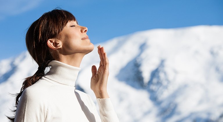 Frau genießt Sonne im Winter mit Schneelandschaft im Hintergrund