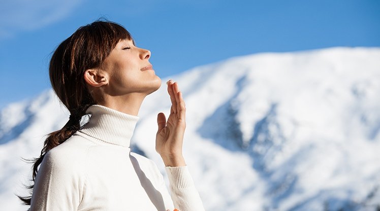 Frau genießt Sonne im Winter mit Schneelandschaft im Hintergrund
