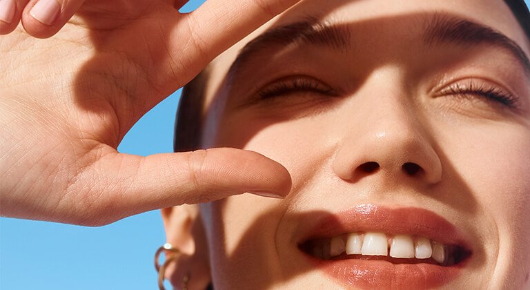 Lächelnde Frau schaut in die Sonne und schirmt ihre Augen mit der Hand ab
