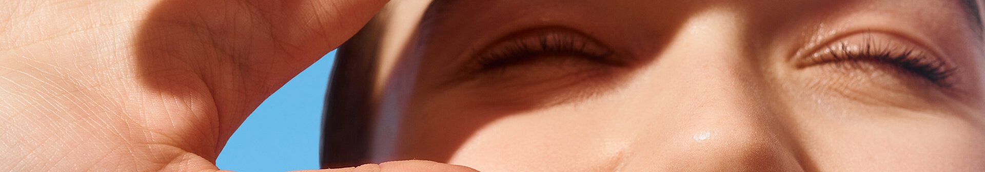 Lächelnde Frau schaut in die Sonne und schirmt ihre Augen mit der Hand ab