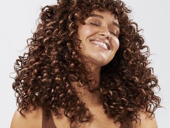 Junge frau mit braunen, lockigen Haaren schwingt die Haare und lächelt.