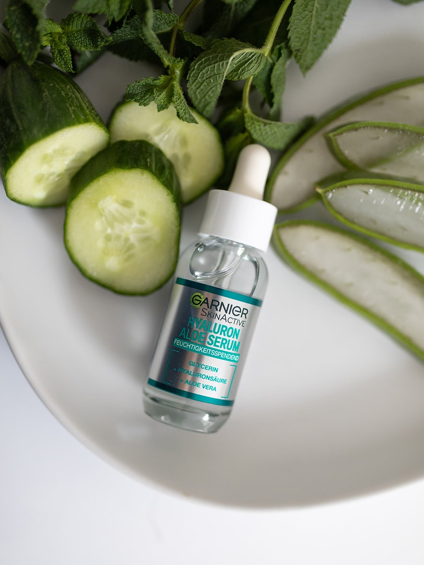 Hyaluron Aloe Serum liegt auf einem Teller zwischen Gurken- und Aloe Vera Streifen