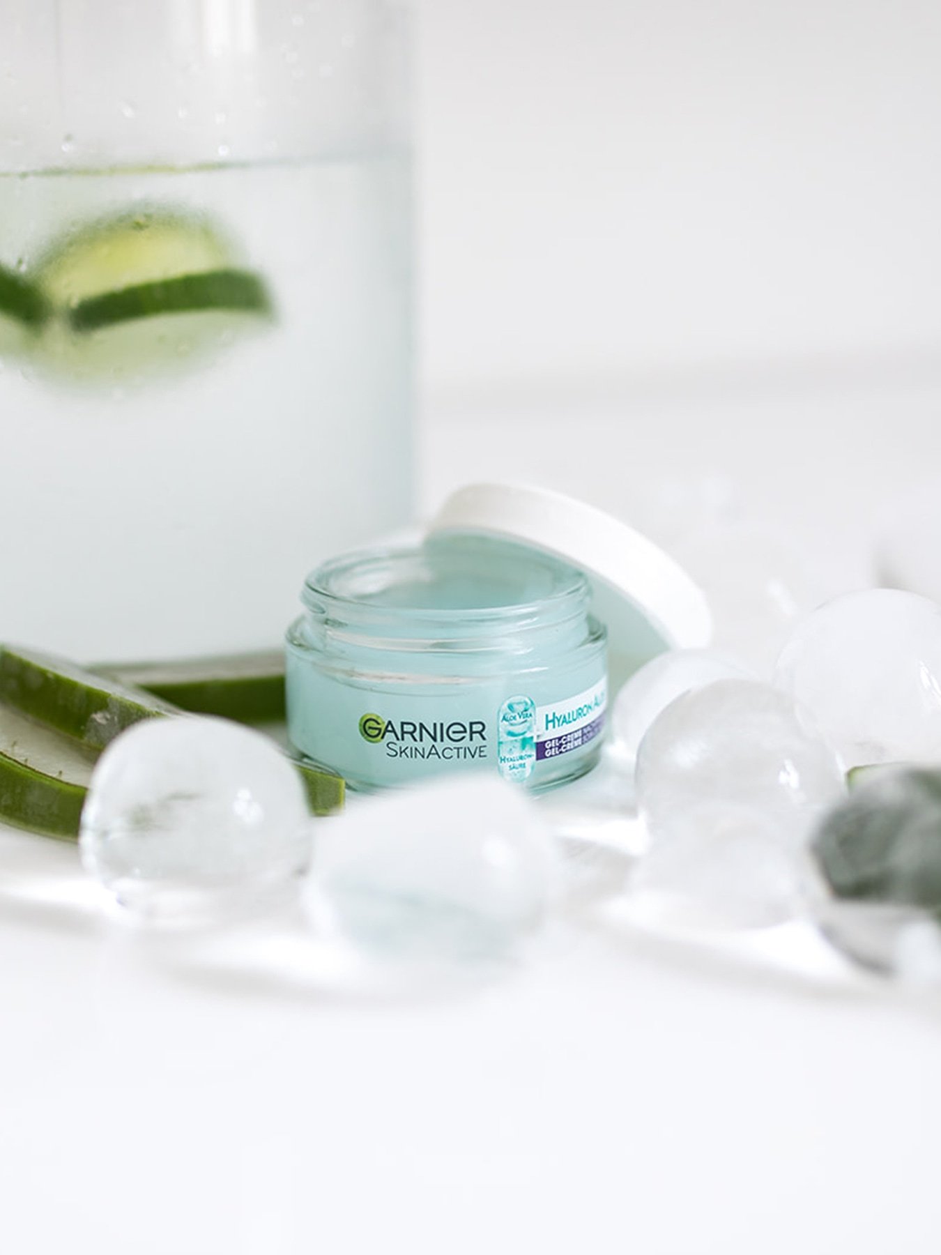 Ein Tiegel Hyaluron Aloe Hydra Booster Gel-Creme Nachtpflege steht zwischen Eiswürfeln und gekühltem Wasser