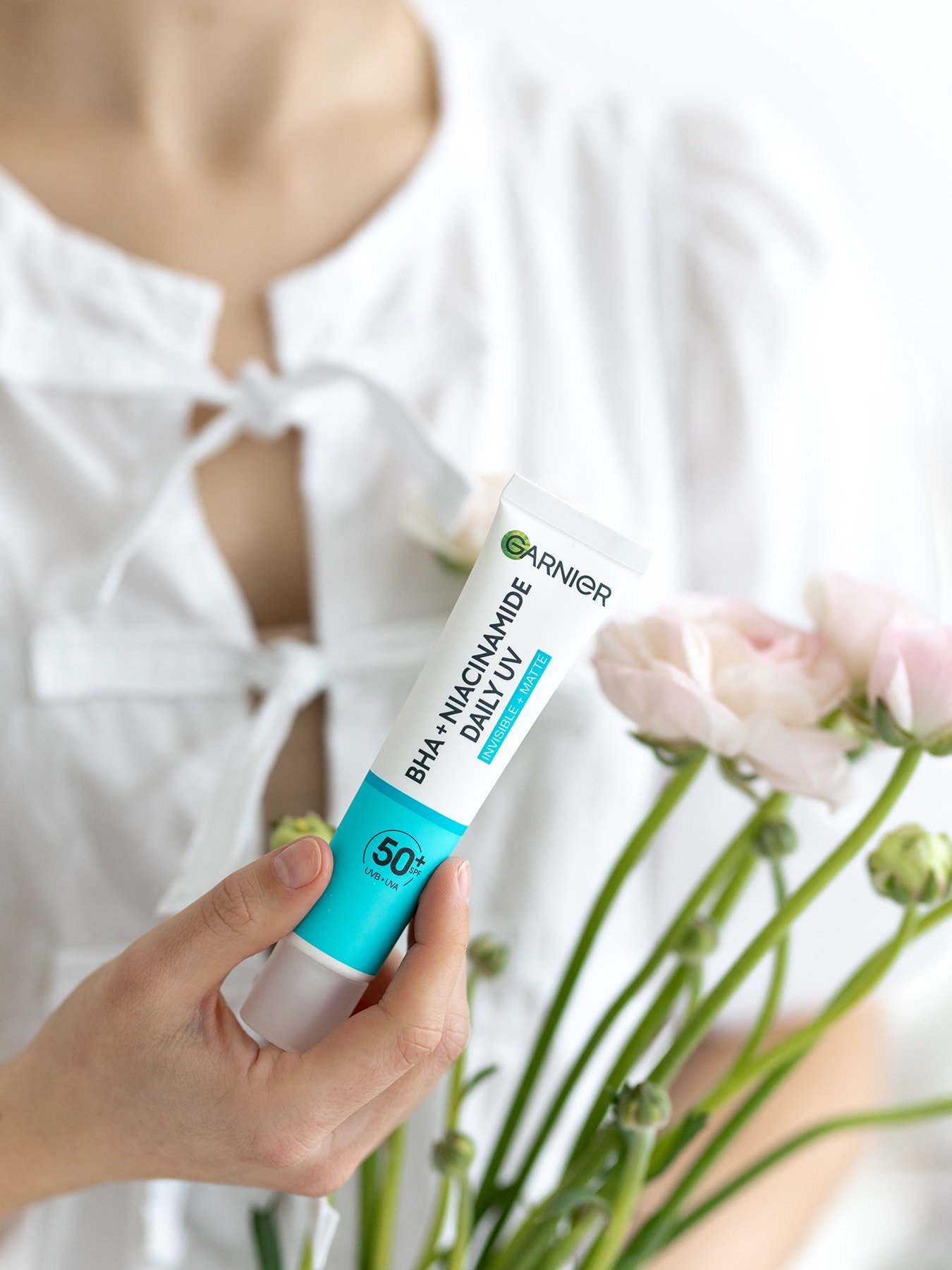 Eine Frau hält eine Tube mit BHA + Niacinamid Daily-UV Anti-Unreinheiten Fluid Invisible in der Hand