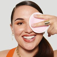 Lächelnde Frau wischt mit einem Reinigungstuch über ihr linkes Auge