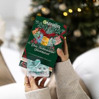 Frau hält SkinActive Tuchmasken 12er Geschenkset in den Händen und im Hintergrund ein Weihnachtsbaum