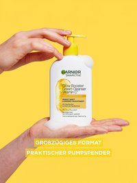 Produkt auf einer Handfläche stehend vor gelben Hintergrund, eine zweite Hand drückt den Spender