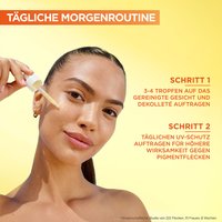 Lächelnde Frau trägt sich Serum aus der Pipette auf die Wange auf