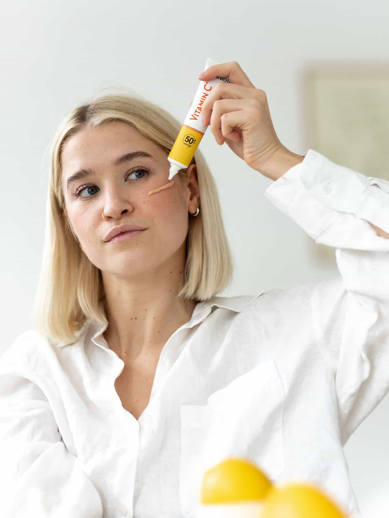 Eine junge Frau trägt auf ihre Wange Vitamin C UV Fluid Glow LSF 50+ auf