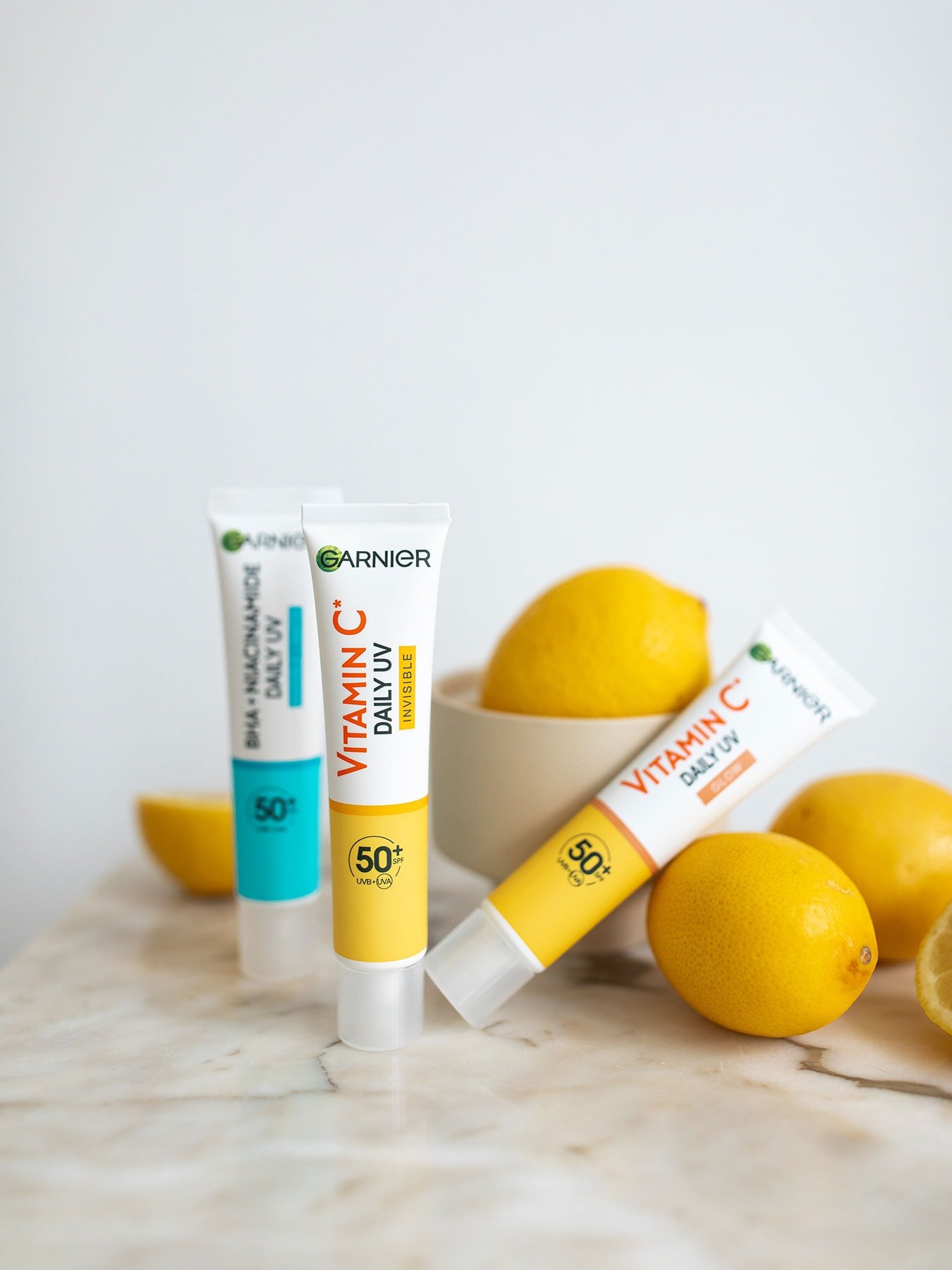 Stillleben mit BHA + Niacinamid Daily-UV, Vitamin C Invisible & Super UV Sonnenfluid und einigen Zitronen