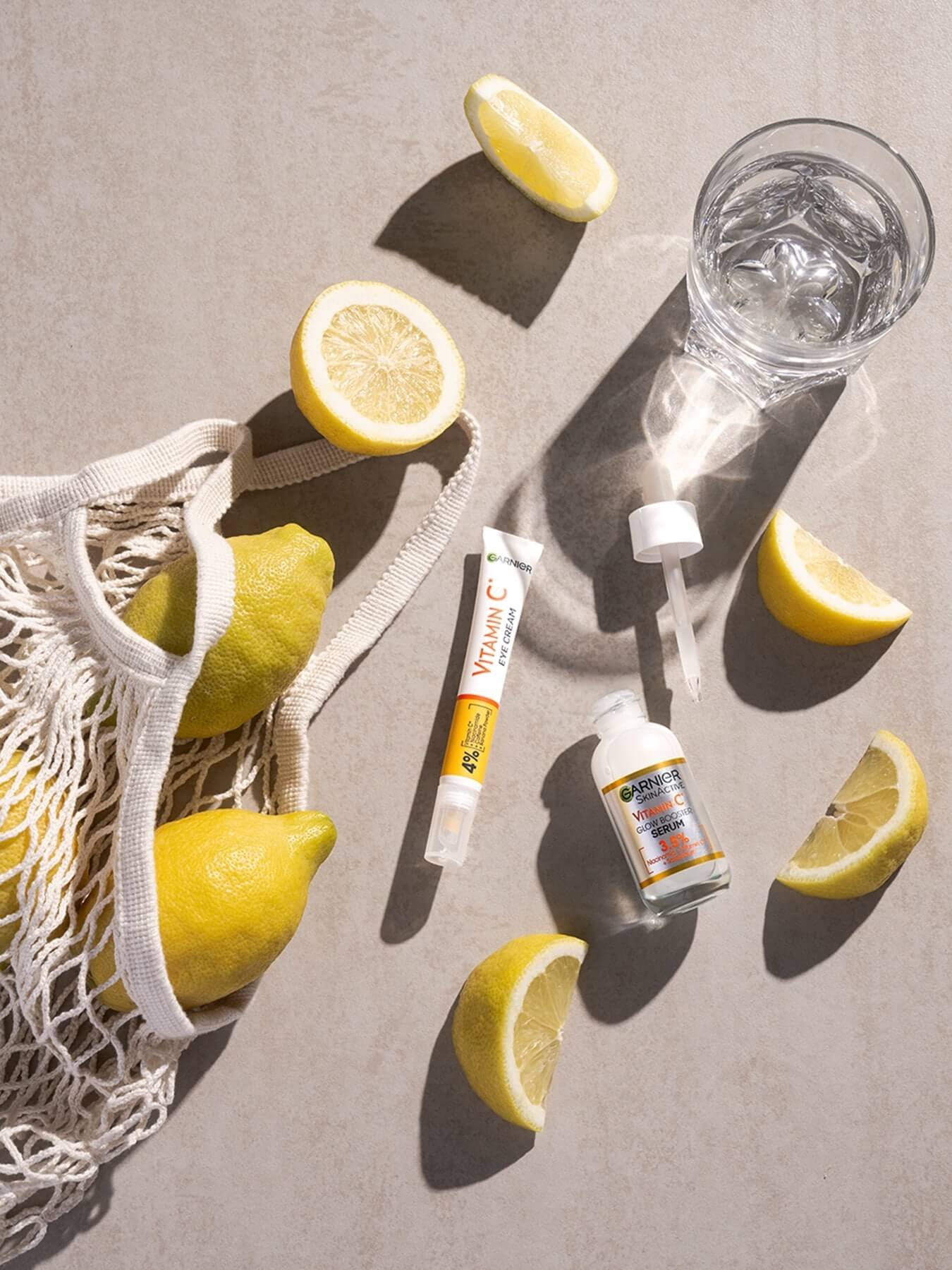 Verschiedene Garnier Vitamin C Pflegeprodukte liegen mit Zitronen neben einer Strandtasche