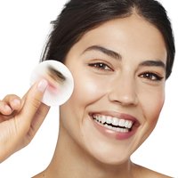 Lächelnde Frau hält ein Reinigungspad voller Make up neben ihr Gesicht